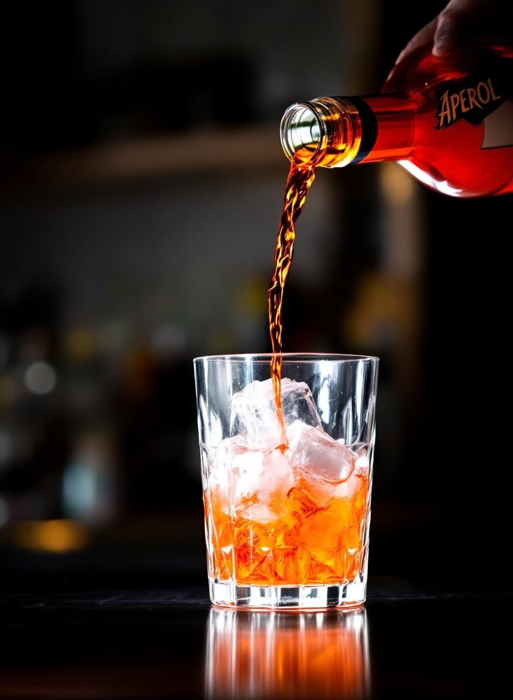 Vibrant Aperol being poured into an ice-filled glass, accentuated by backlighting and ambient bar lighting