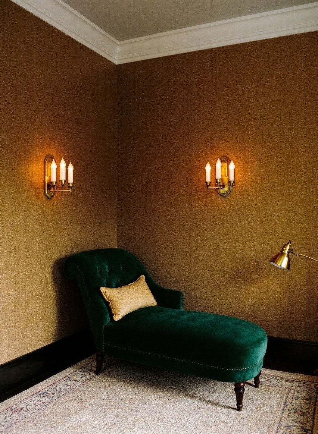 Vintage corner with emerald velvet chaise lounge, textured grasscloth wallpaper, art deco-style sconces, and brass pharmacy lamp in a moody atmosphere