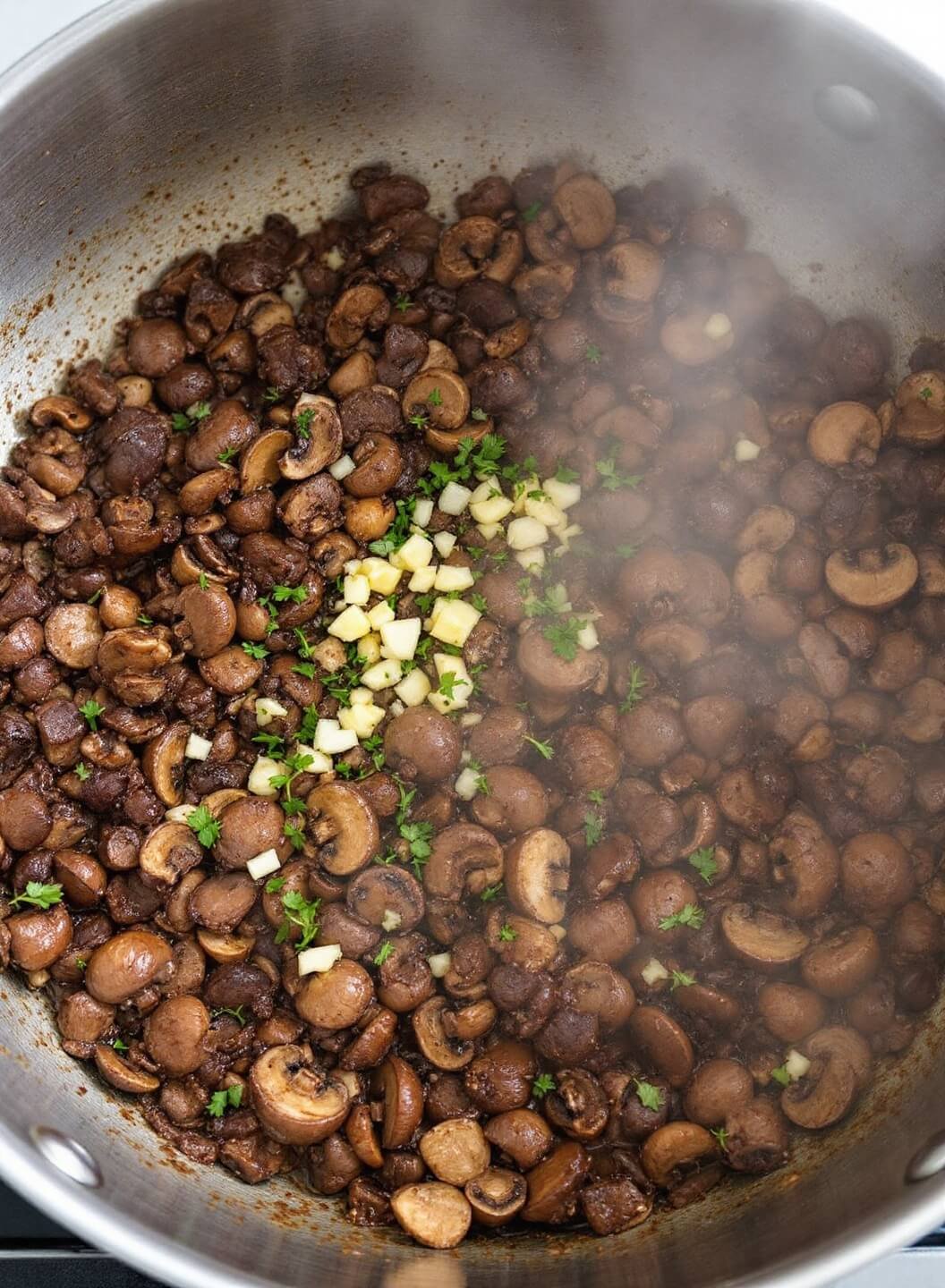 Finely chopped mushrooms, butter, and shallots reducing in a pan, with fresh herbs and minced garlic visible