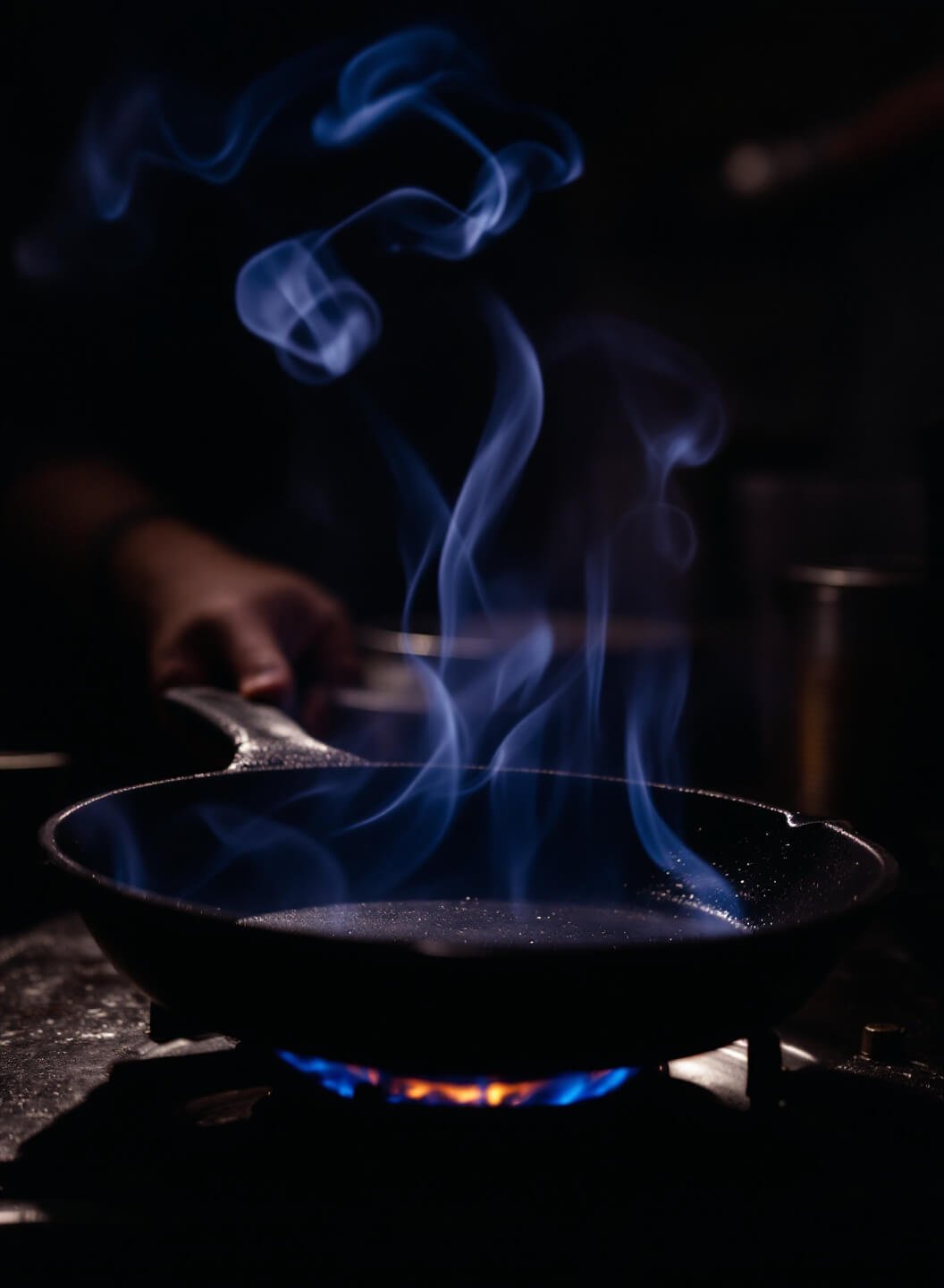 Dramatic shot of a smoking hot cast iron skillet in a professional kitchen, highlighted by intense lighting with visible flame underneath