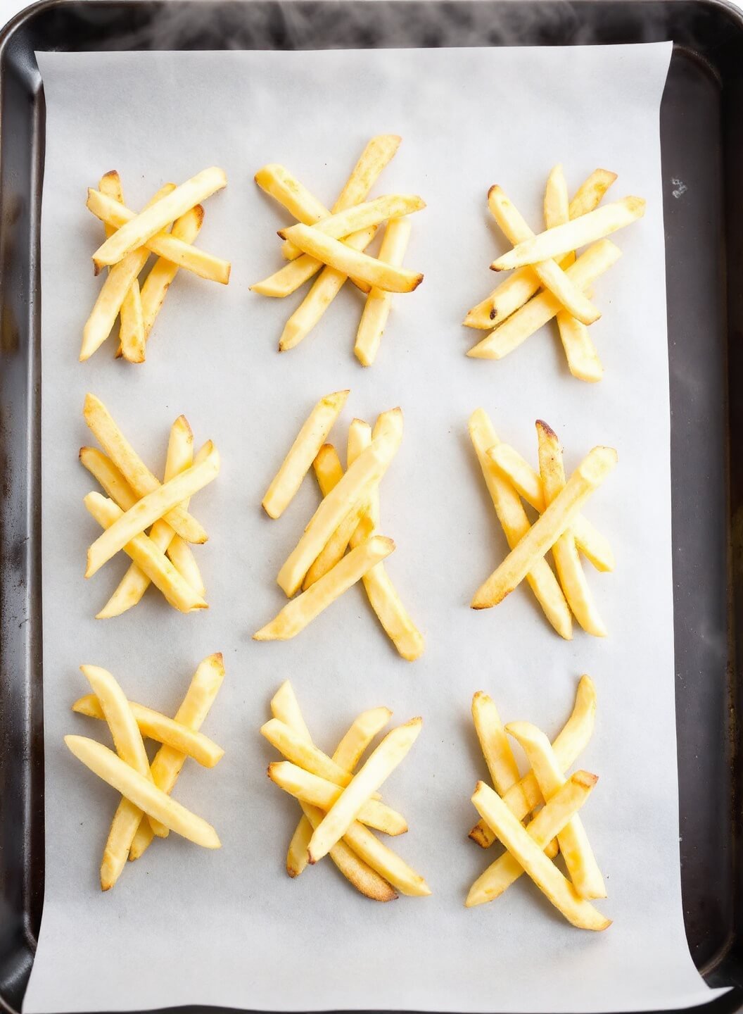 Golden fries perfectly spaced on parchment paper with steam rising under professional kitchen lighting.