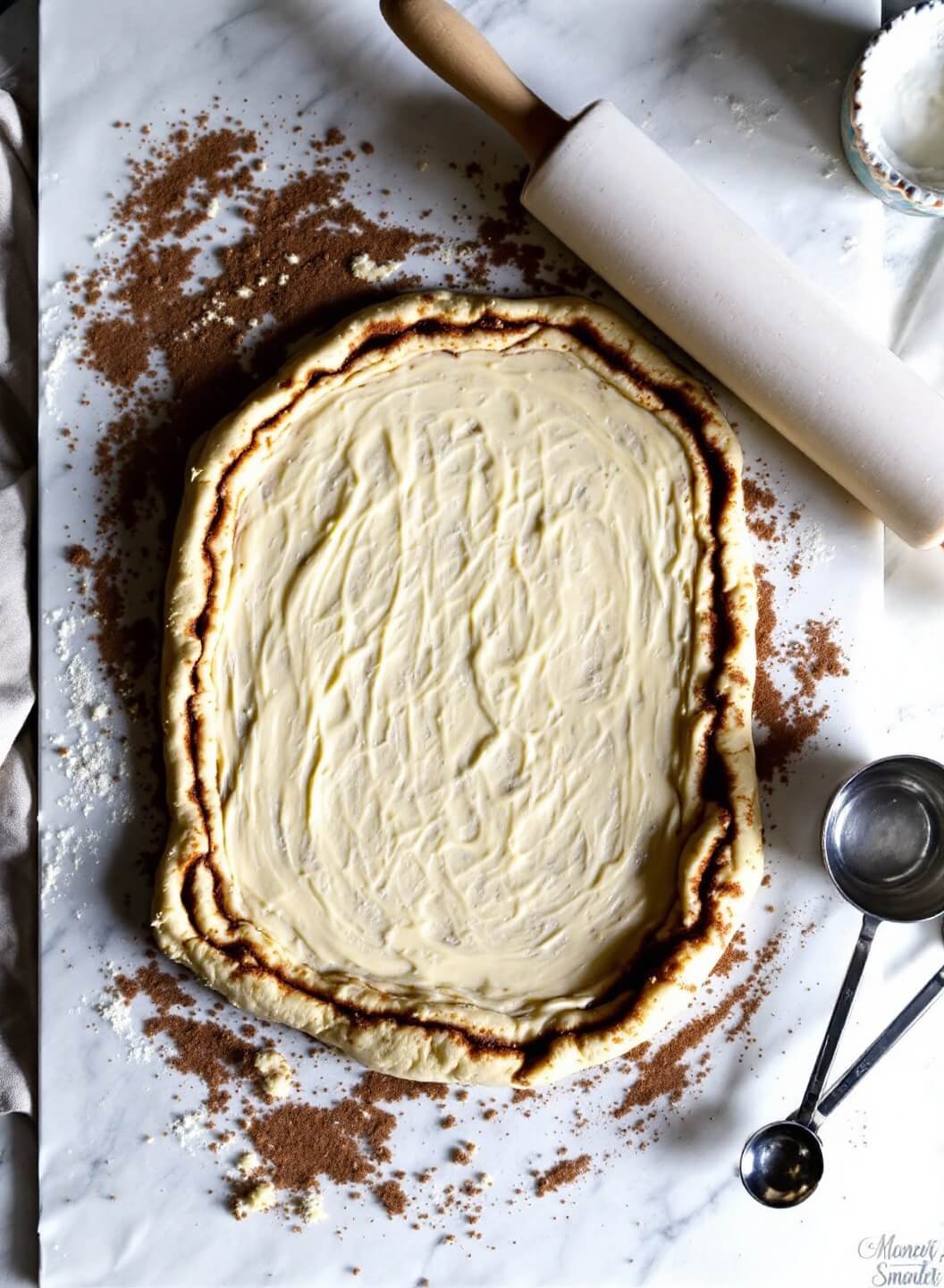 Overhead view of rectangular dough coated with cinnamon-sugar, alongside vintage rolling pin and measuring spoons