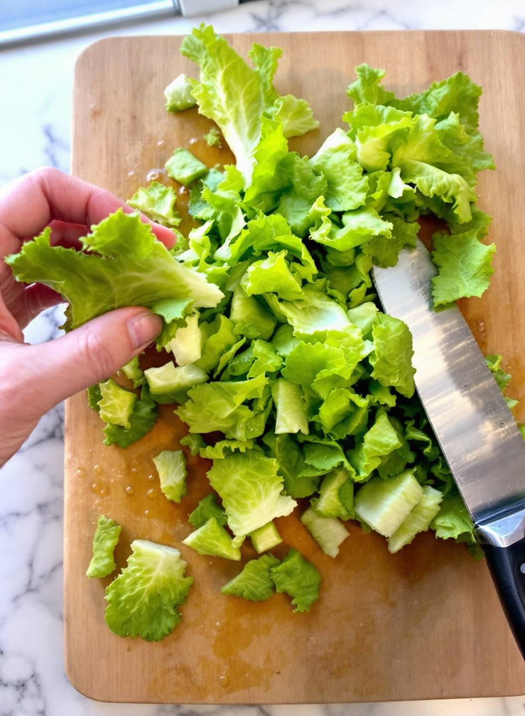 Fresh romaine leaves being torn into bite-sized pieces on a wooden cutting board, highlighted by natural window light