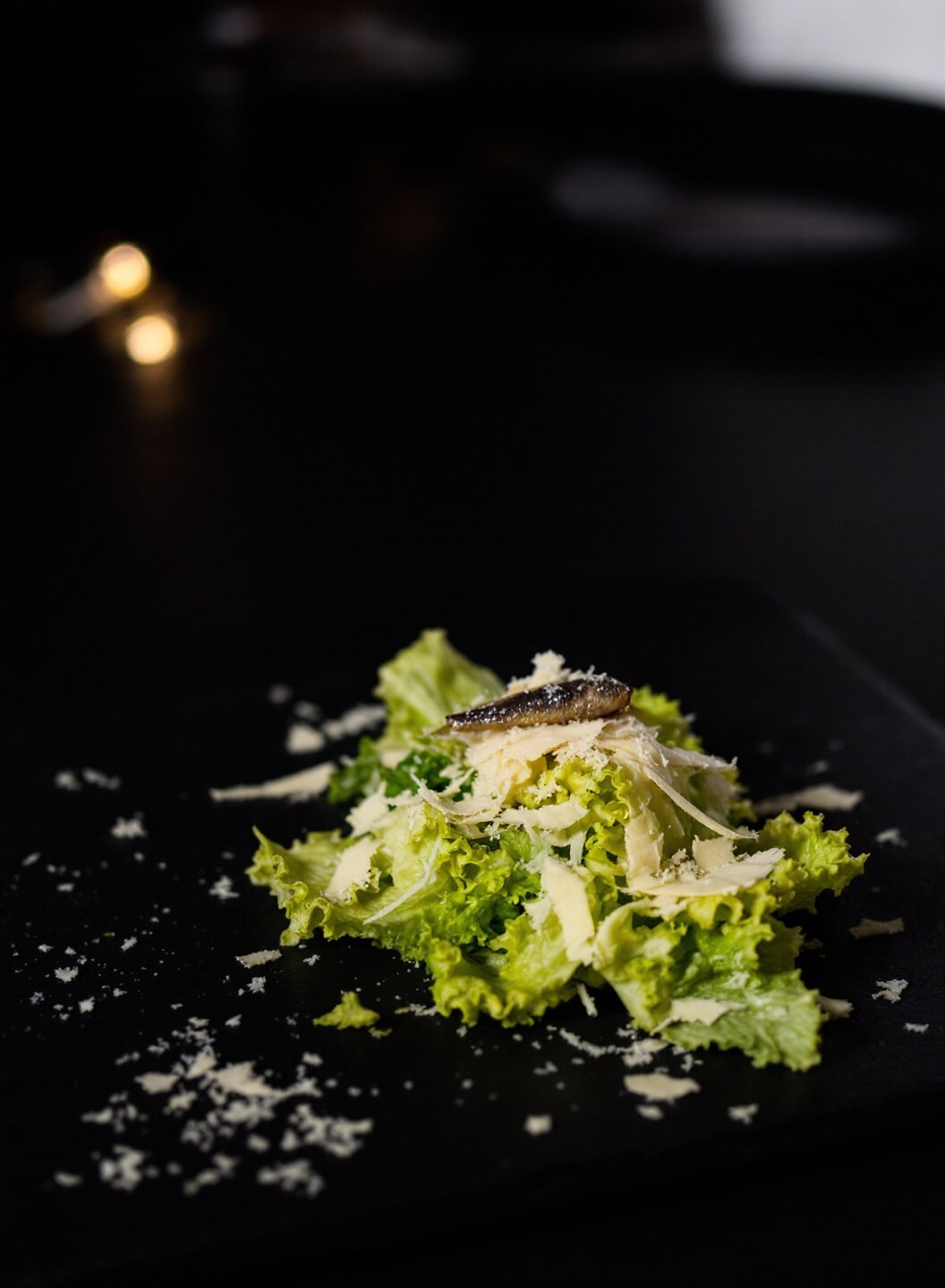 Completed Caesar salad garnished with Parmesan and anchovy under restaurant lighting