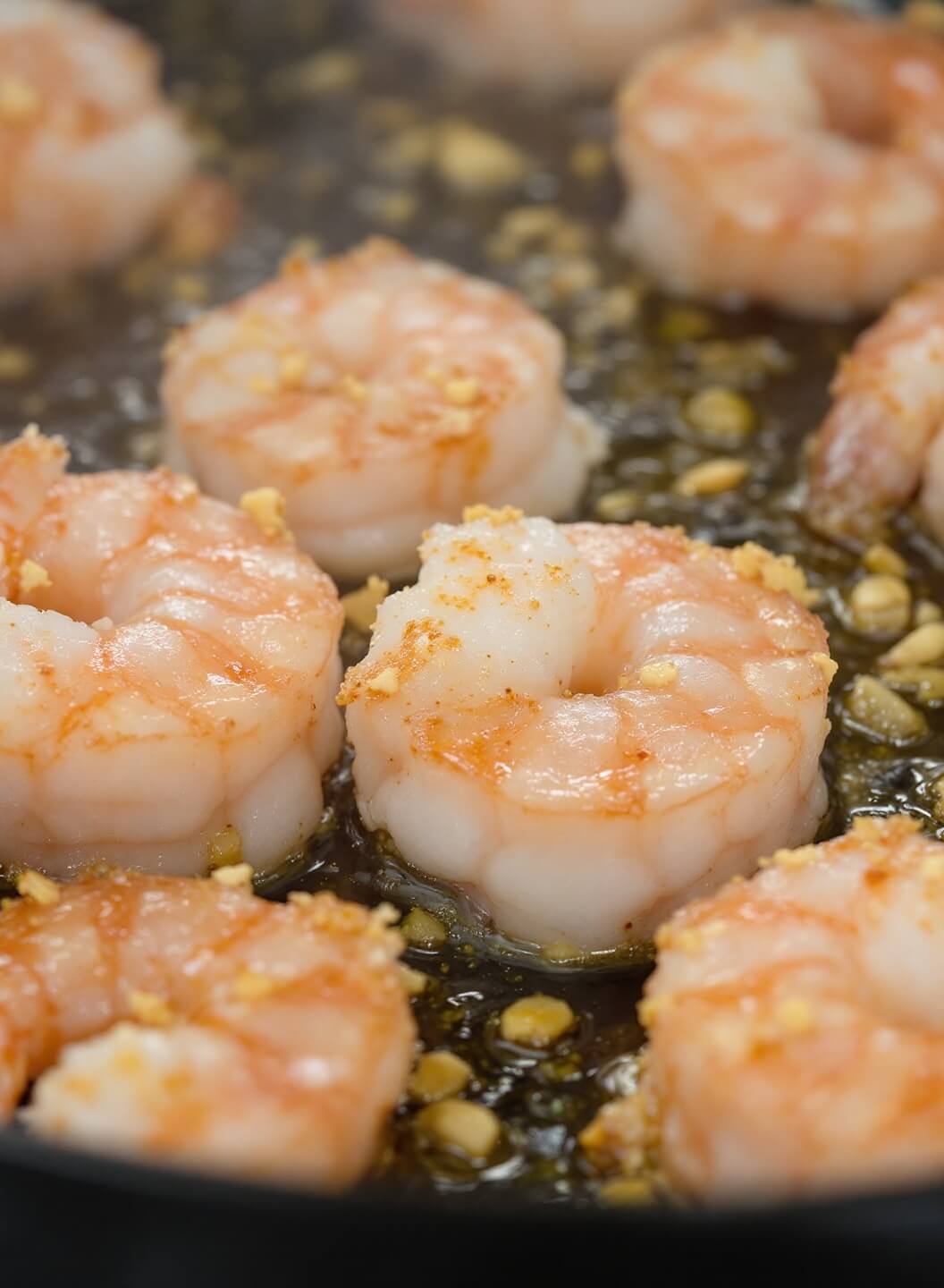 Large pink shrimp searing in butter with garlic, showing caramelization under natural kitchen lighting