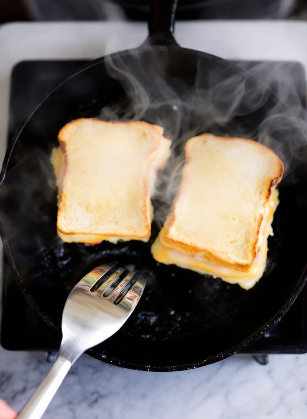 Two sandwiches cooking in a cast-iron skillet with steam rising, butter bubbling, and cheese melting