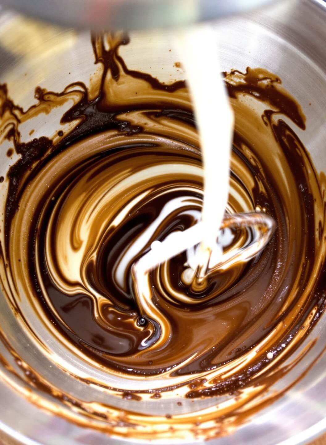 Chocolate cake batter being mixed in a stainless steel bowl with streams of coffee and buttermilk.