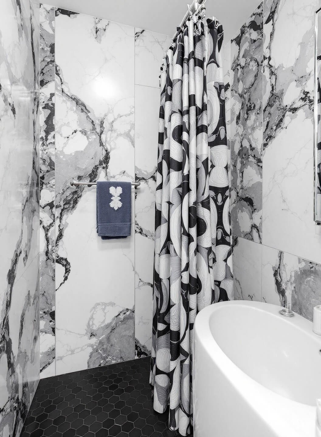 Contemporary 5x8 ft bathroom with grey and white marble-effect tiles, matte black penny tile floor, and slate blue and silver shower curtain, shot at an angle to show mirror reflection with dramatic artificial lighting.