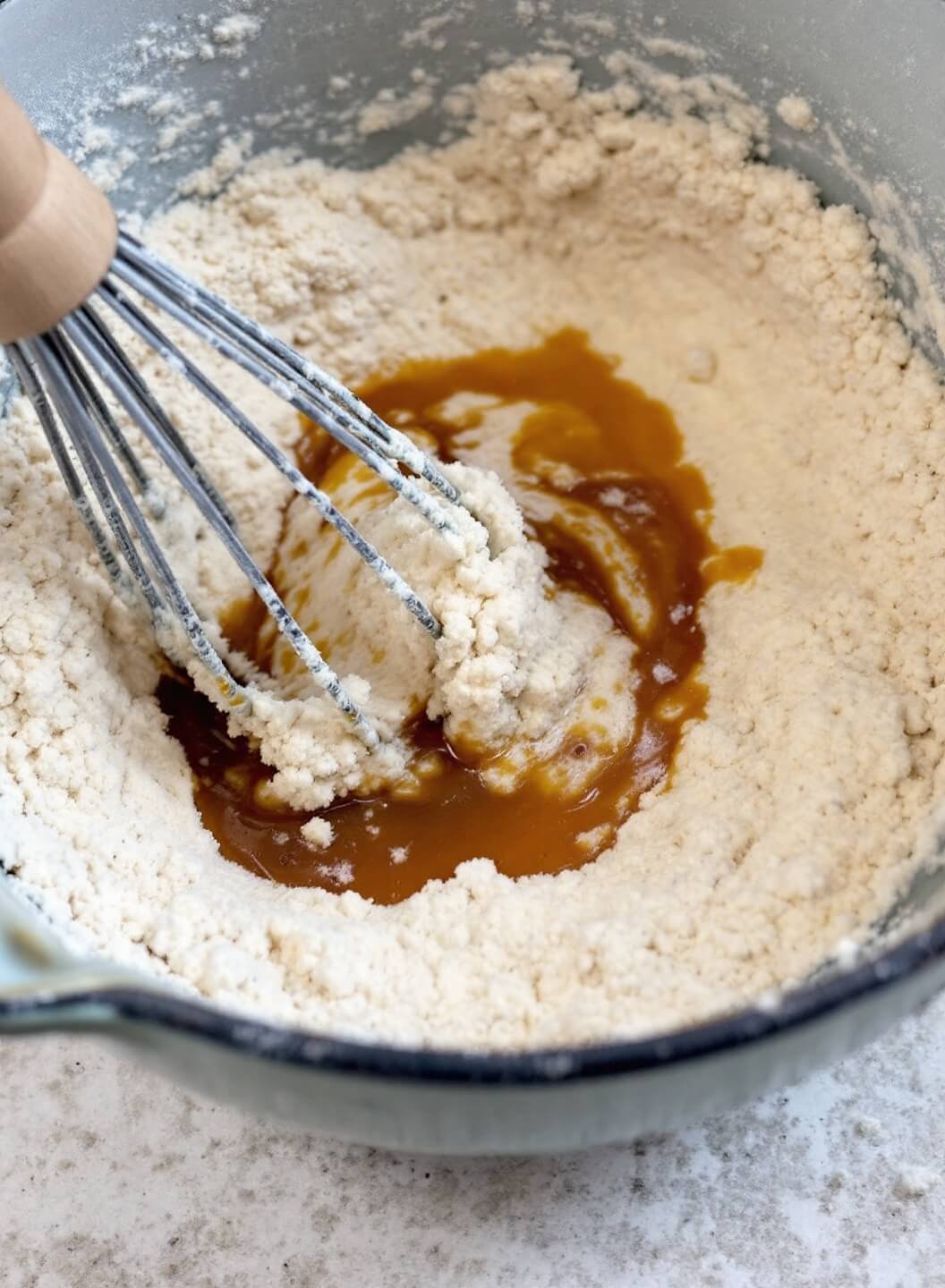 Close-up view of pancake batter being mixed with a wooden whisk in a vintage ceramic bowl