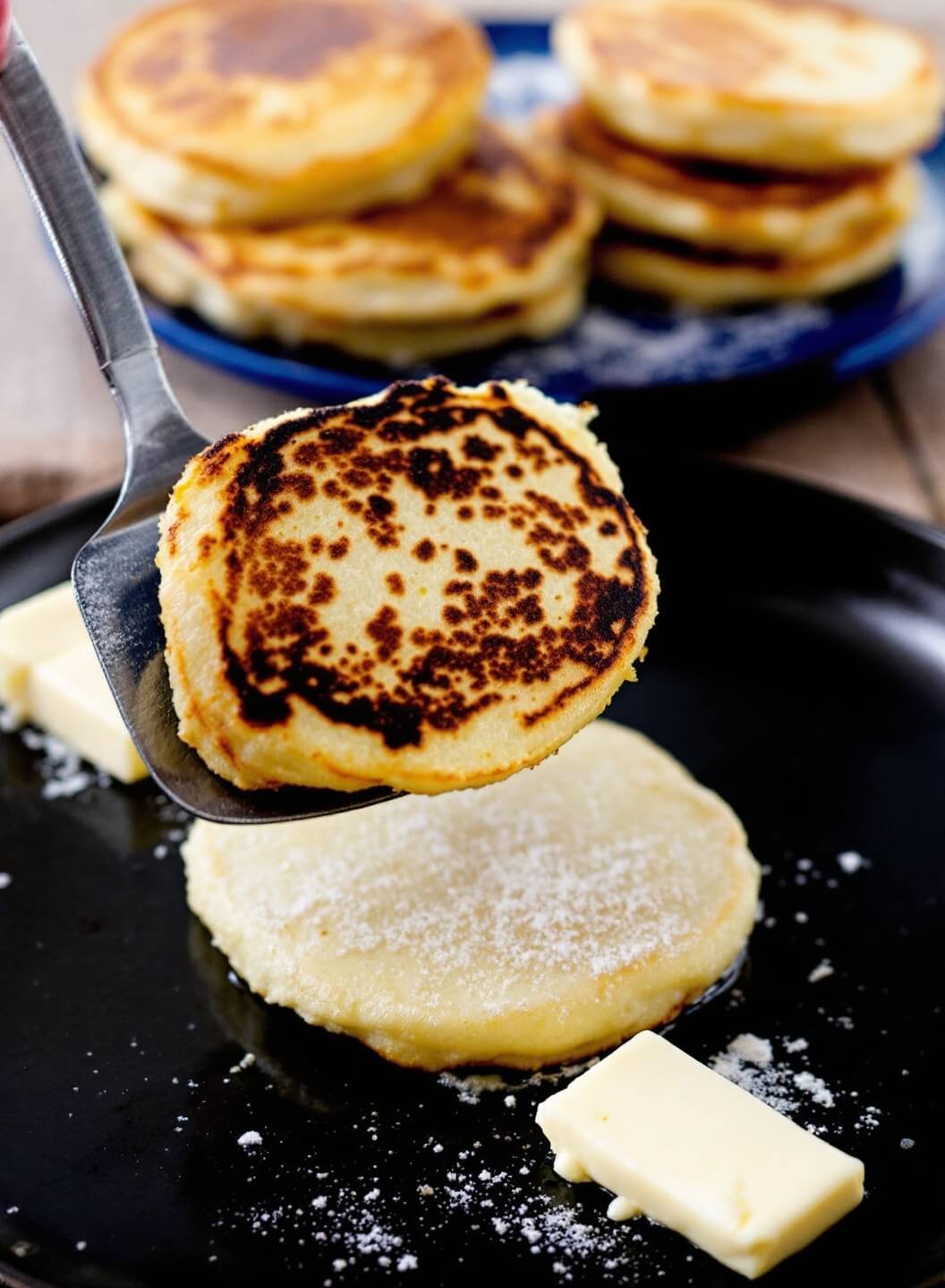 Spatula flipping a golden-brown pancake mid-air with melted butter on cooked stack in the background