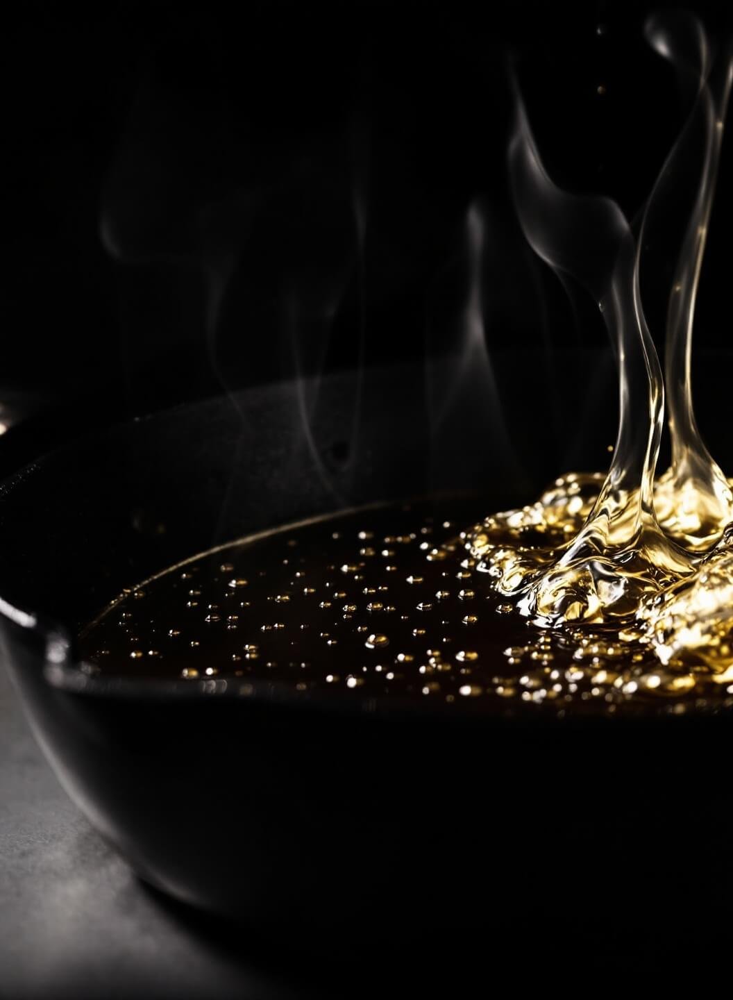 Hot oil shimmering in a seasoned black cast-iron skillet with an analog thermometer showing 350°F, steam rising against a dark background