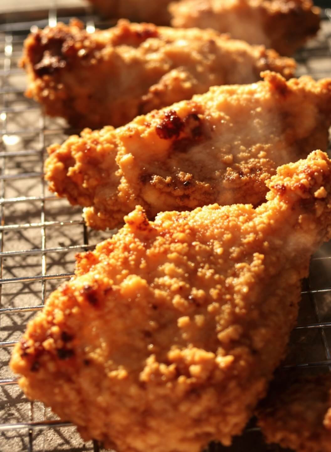 Golden-brown fried chicken pieces on a wire rack with visible steam and crispy texture, under warm afternoon light