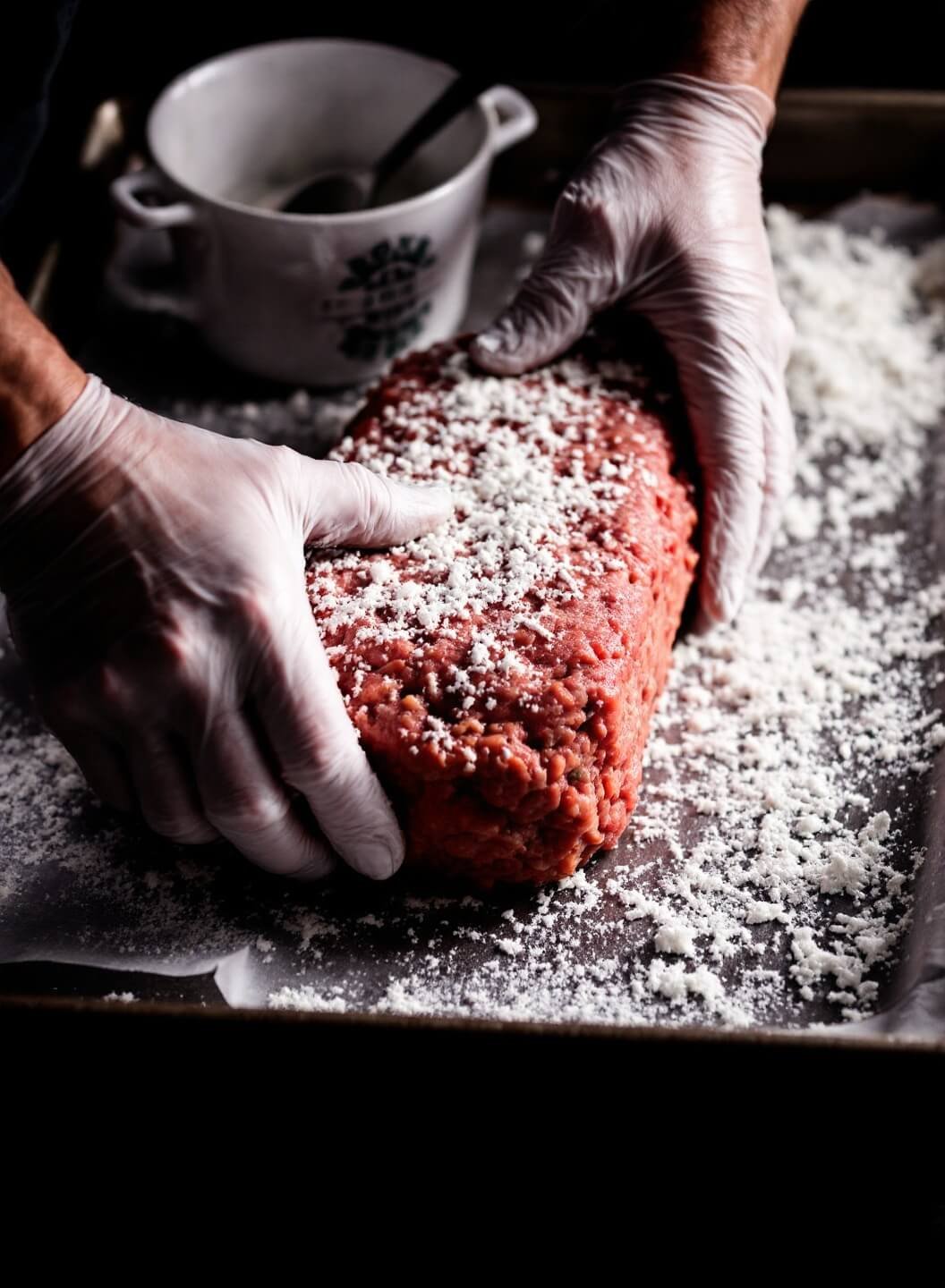 Artisan hands shaping a perfect loaf of meatloaf on a professional baking sheet, highlighted by dramatic side lighting showcasing its texture