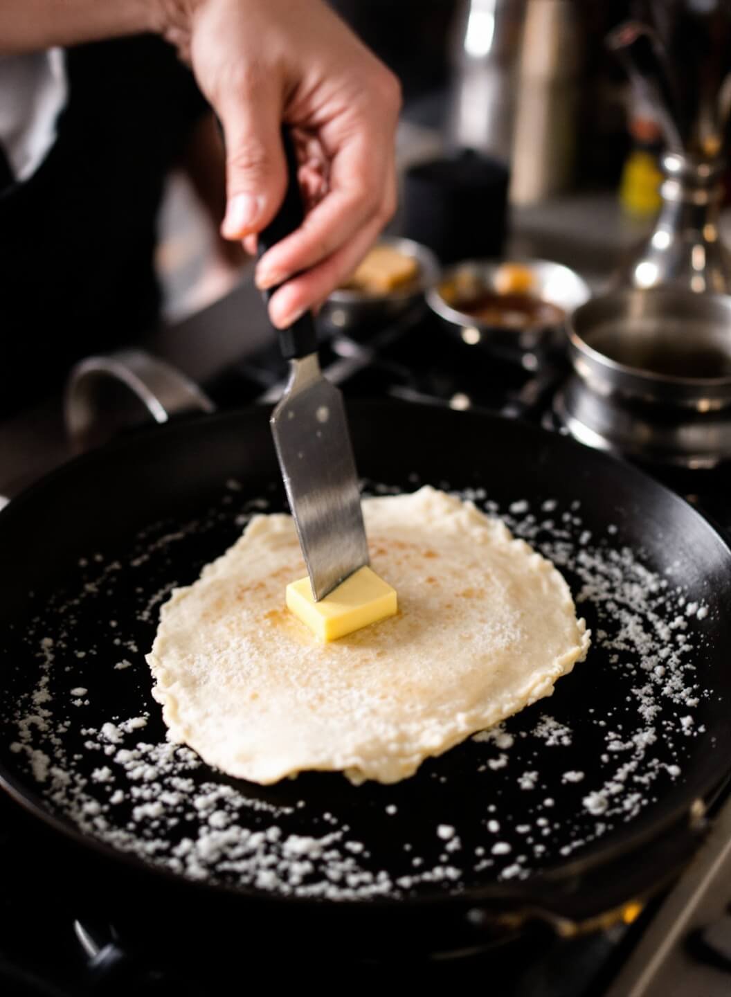 Action shot of a perfect crepe flip with lacy edges in a warm kitchen atmosphere, with sizzling butter.