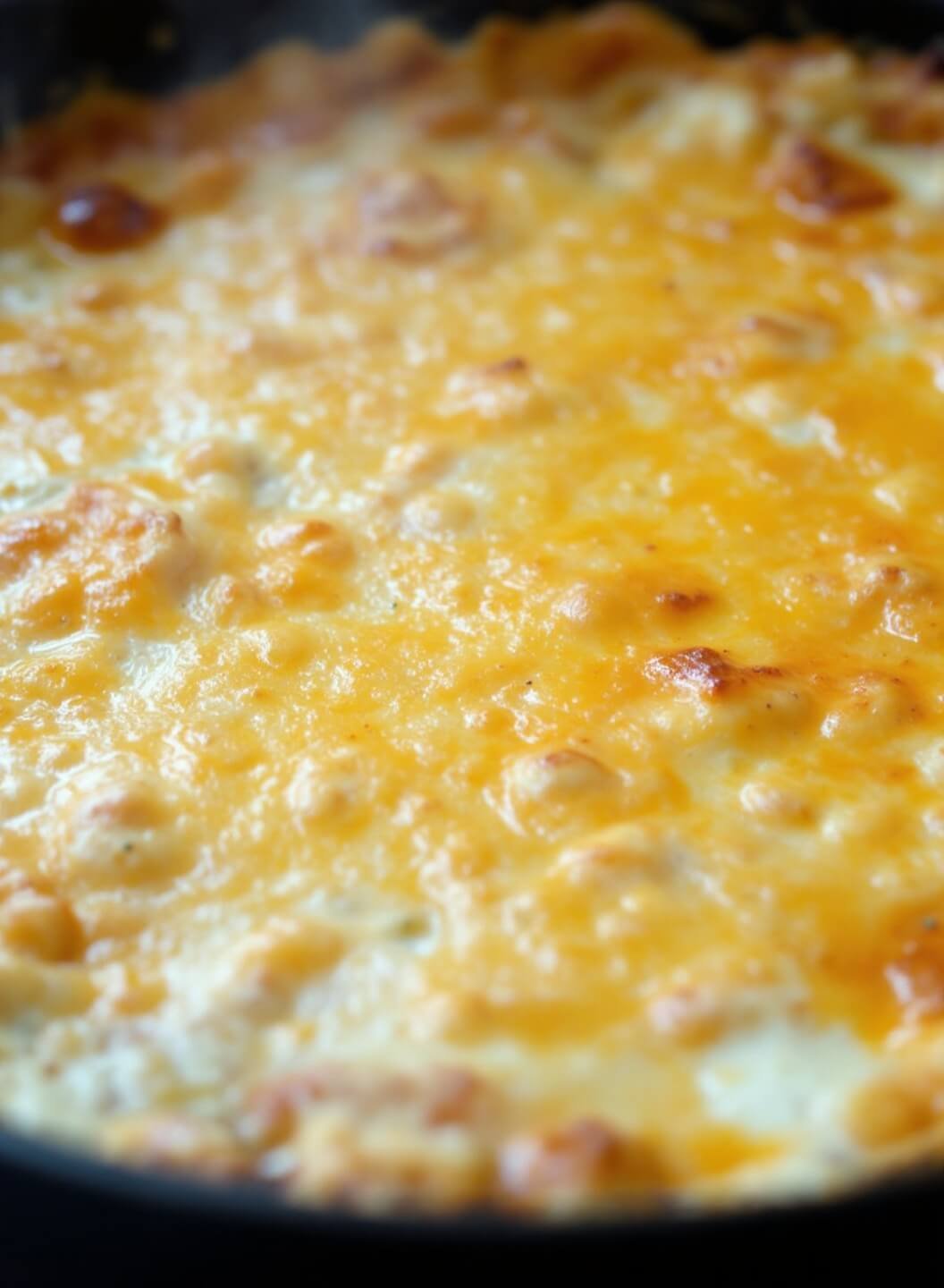 Close-up of freshly baked dip with bubbling golden-brown edges and melted cheese, steam rising under warm light.