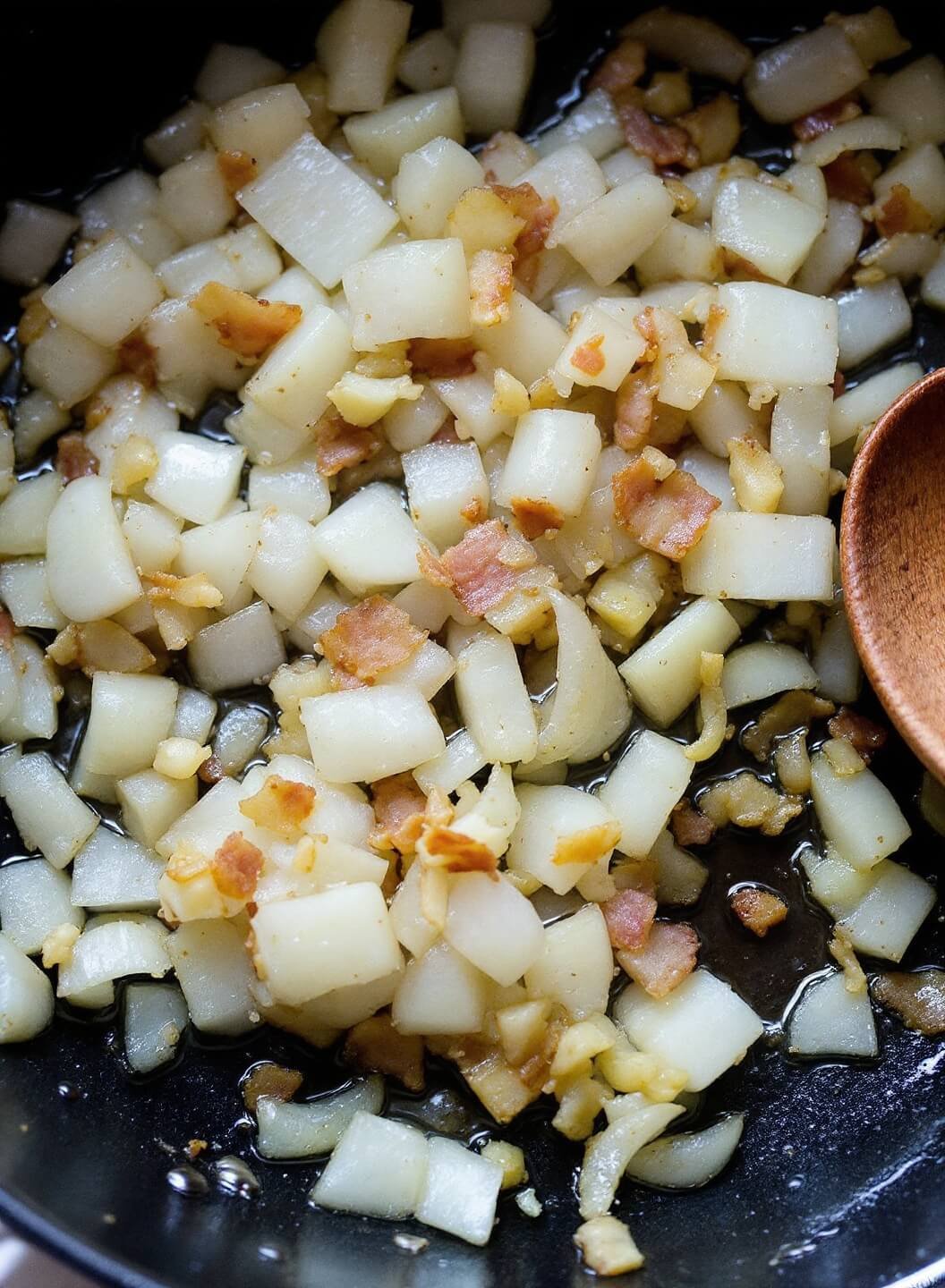 Caramelizing diced onions and minced garlic in bacon drippings with wooden spoon on side