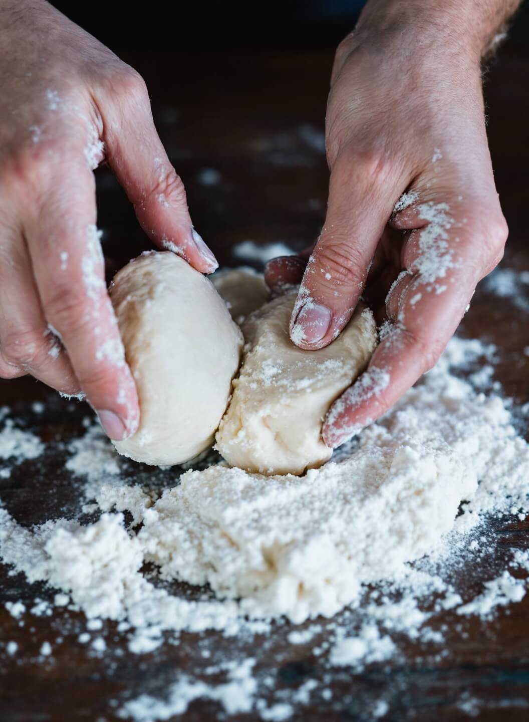 Artisanal hands gently shaping marbled butter dough into a smooth disk on a rustic wooden surface, with a light dusting of flour visible in the air