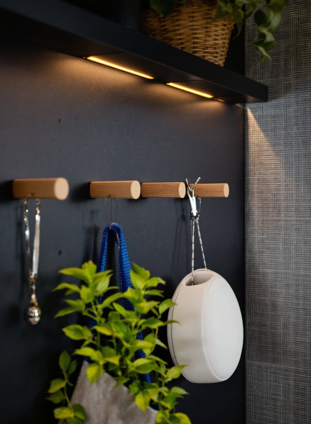 Custom black pegboard system with wooden pegs holding items against gray grasscloth wallpaper in evening light