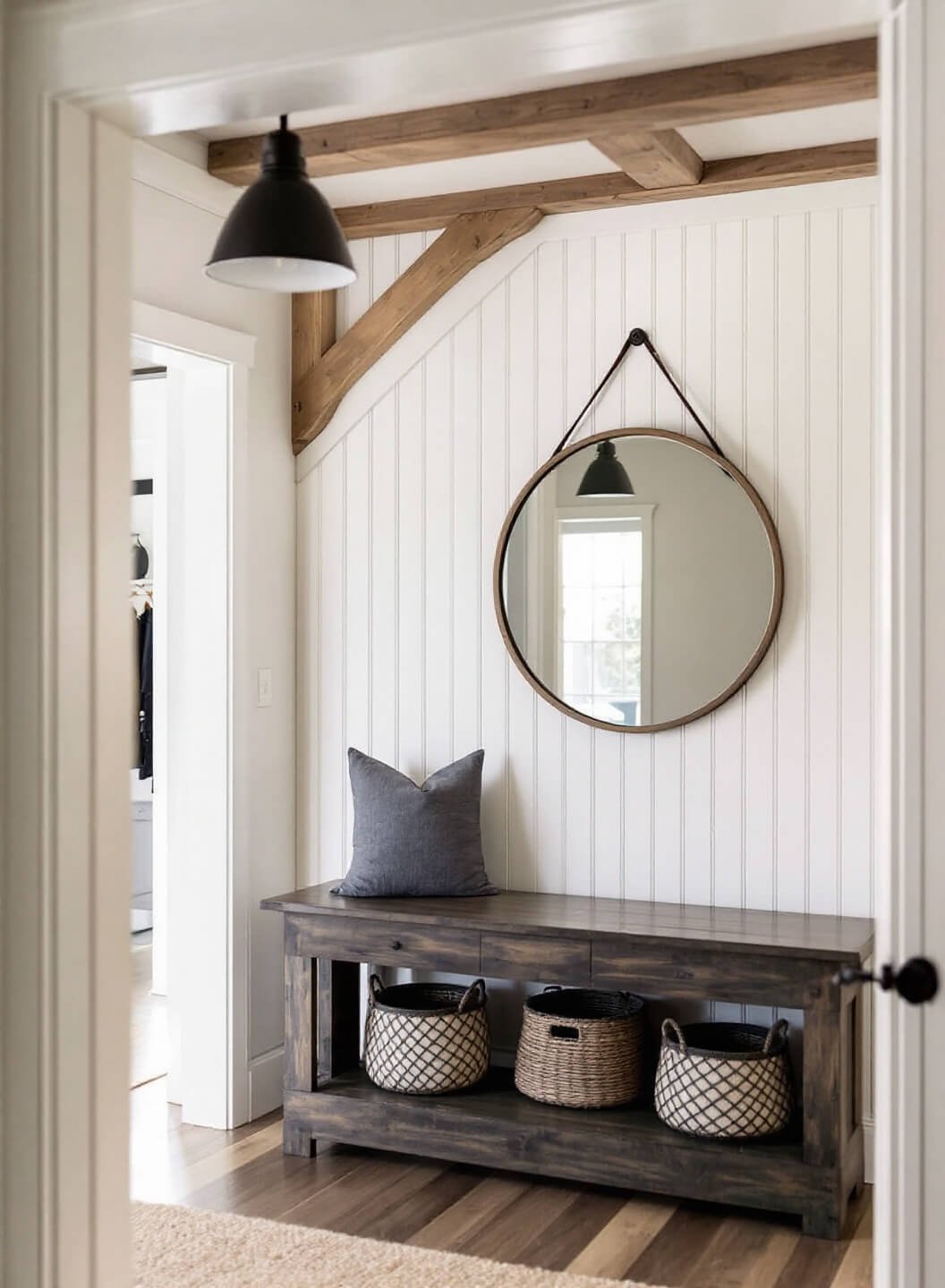 Sunrise illuminating a modern farmhouse entryway with white shiplap walls, rustic wood beams, a black pendant light, distressed wood bench with woven baskets underneath, and a large round mirror reflecting the morning light