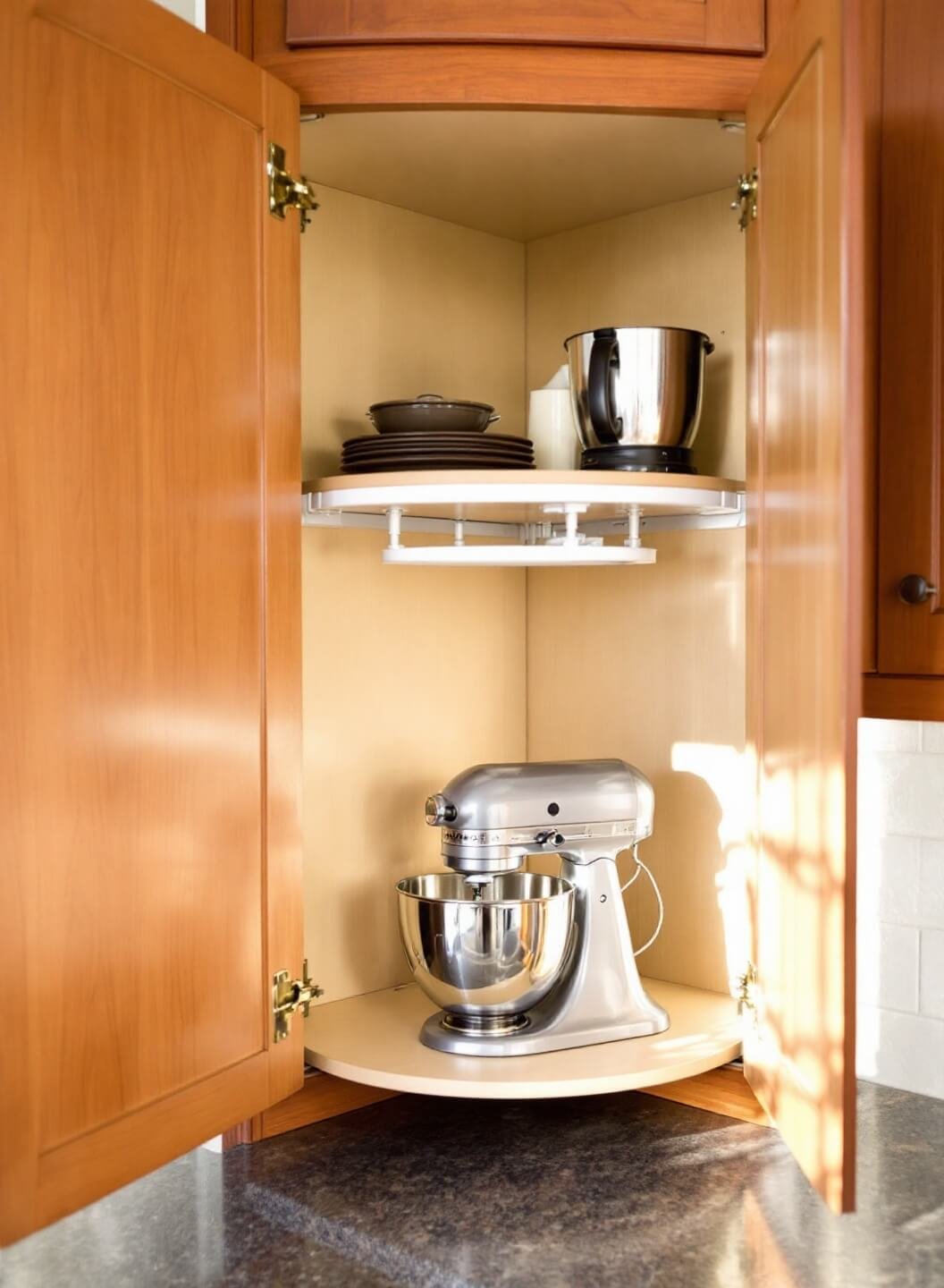 Overhead view of a cherry wood corner cabinet with a rotating lazy susan, featuring a KitchenAid stand mixer and smaller appliances, highlighted by late afternoon light.