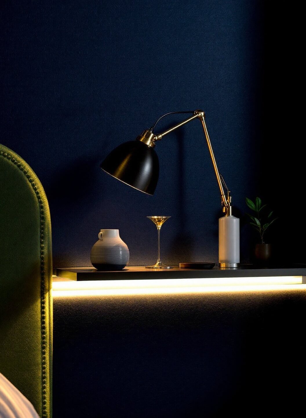 Modern brass reading light on navy grasscloth wallpaper with under-shelf LED strips illuminating displayed objects in warm evening light, shot at f/2 for depth of field