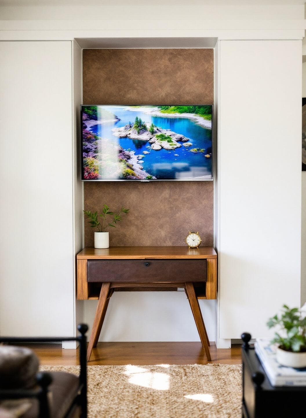 Lifestyle vignette featuring a leather storage bench, small desk used as nightstand and hidden wall-mounted TV behind sliding art panel in warm afternoon natural light.