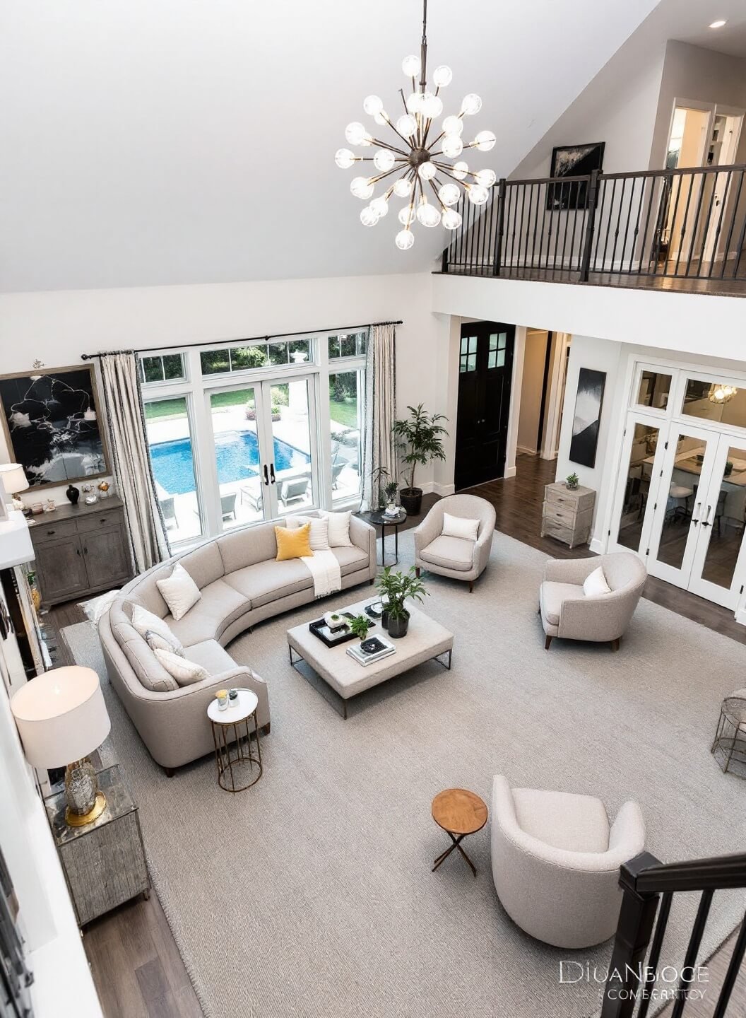 Modern great room with cathedral ceiling, multiple conversation areas defined by large neutral rugs, featuring a curved sofa, swivel chairs and a sputnik chandelier, viewed from a mezzanine with a balanced mix of natural and artificial lighting.